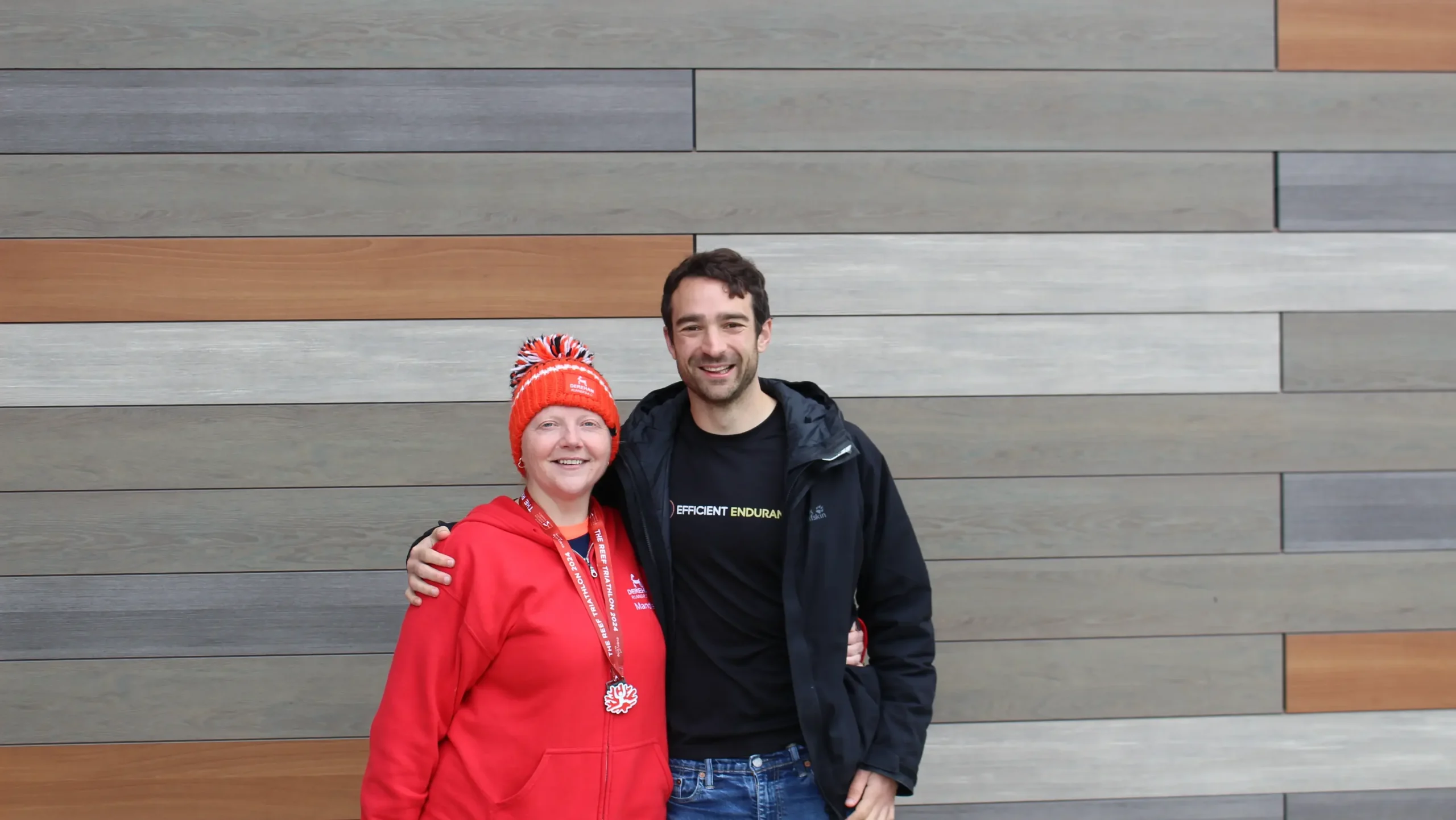 A female wearing red and a red bobble hat with a medal with her triathlon coach