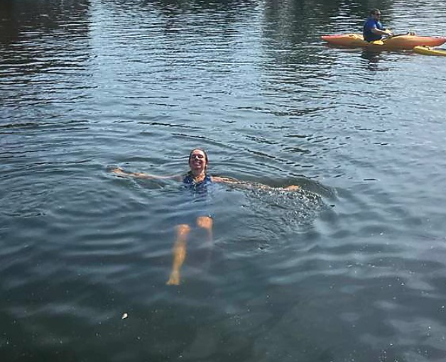 The same swimmer on their back in a river, smiling.