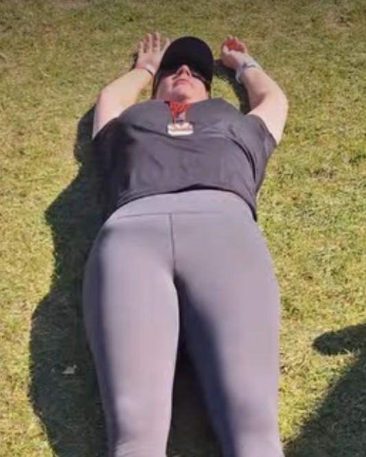 Athlete laying on the floor arms stretched above their head with a medal on their chest.