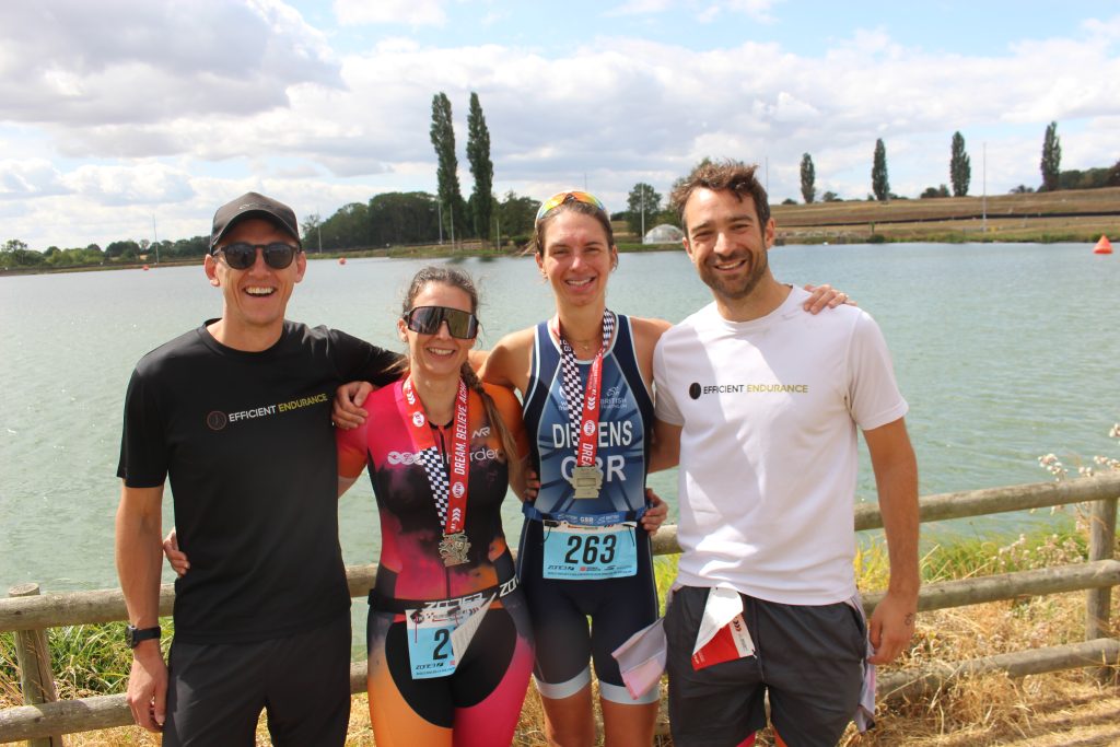 4 efficient endurance athletes after the mallory park sprint trip with their medals in front of the lake.